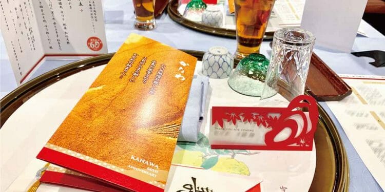 企業の設立記念パーティー用の和食献立のメニュー表と企業の沿革を印刷したパンフレットと牡蠣と紅葉がカッティングされた赤い台紙の席札
