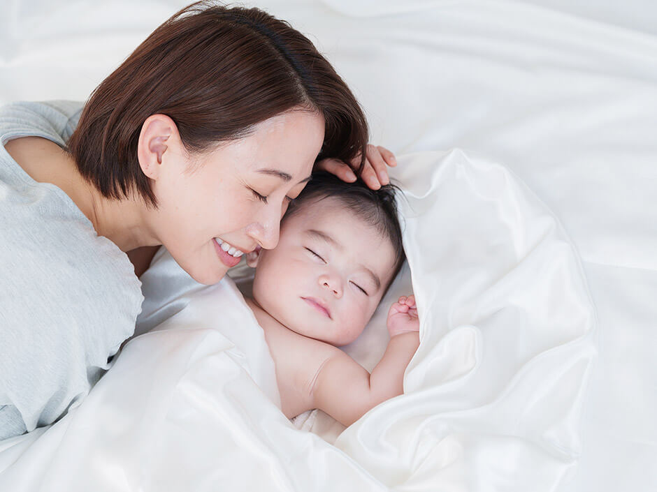 寝ている赤ちゃんに寄りそう笑顔の母親