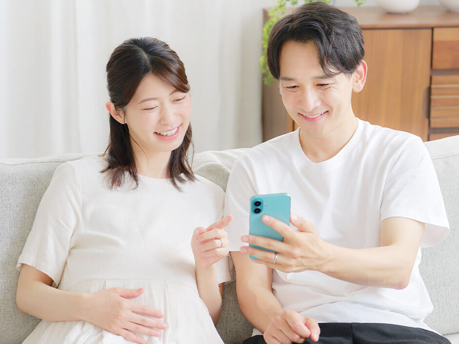 スマホで命名書を選んでいる笑顔のプレママ・パパ