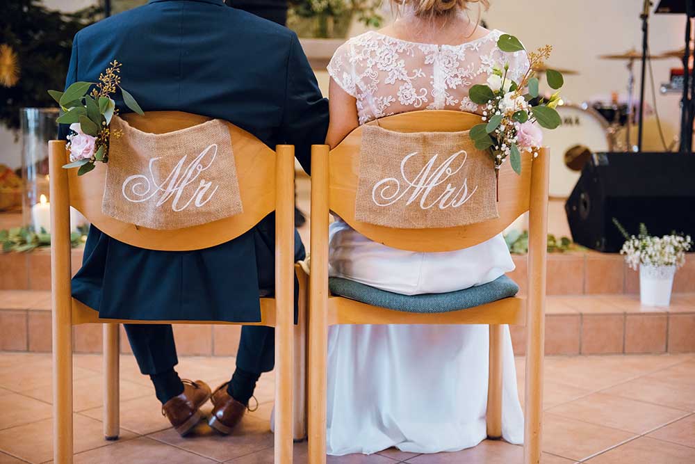 MrMrsというチェアサインで飾り付けた椅子に座る新郎新婦
