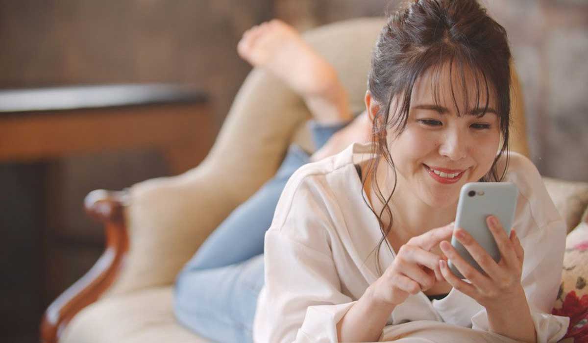 ベッドに寝転んでスマホを触っている女性