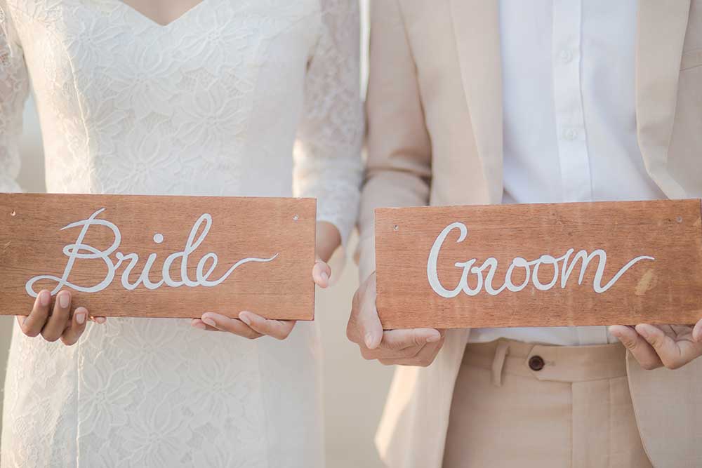 木製のGroomBrideサインを手に持つ新郎新婦