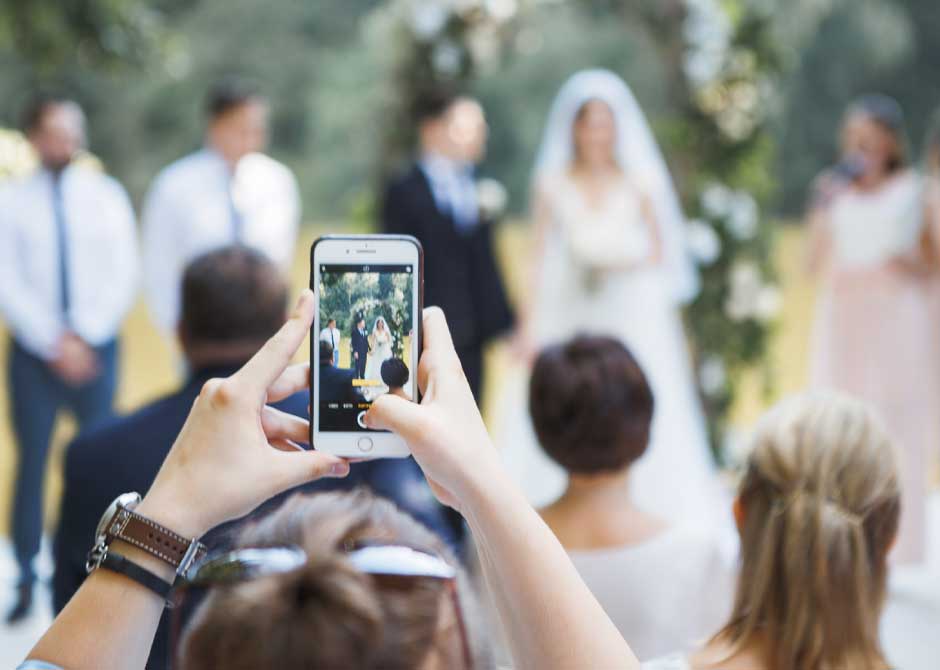 スマホで新郎新婦の写真を撮っている結婚式のゲスト