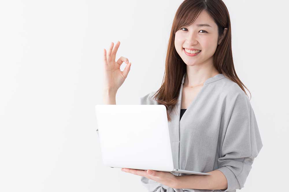 パソコンを手に持ちOKサインをする女性