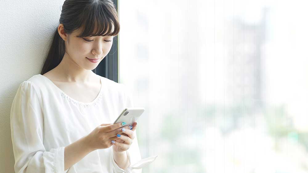 壁に寄りかかってスマホを操作している女性