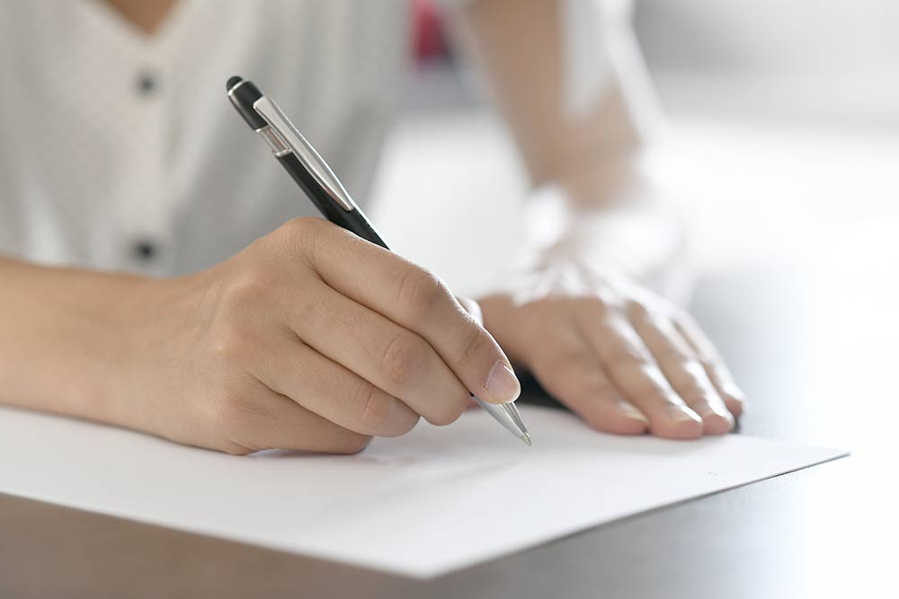 便箋にペンで手紙を書いている女性の手元をクローズアップ