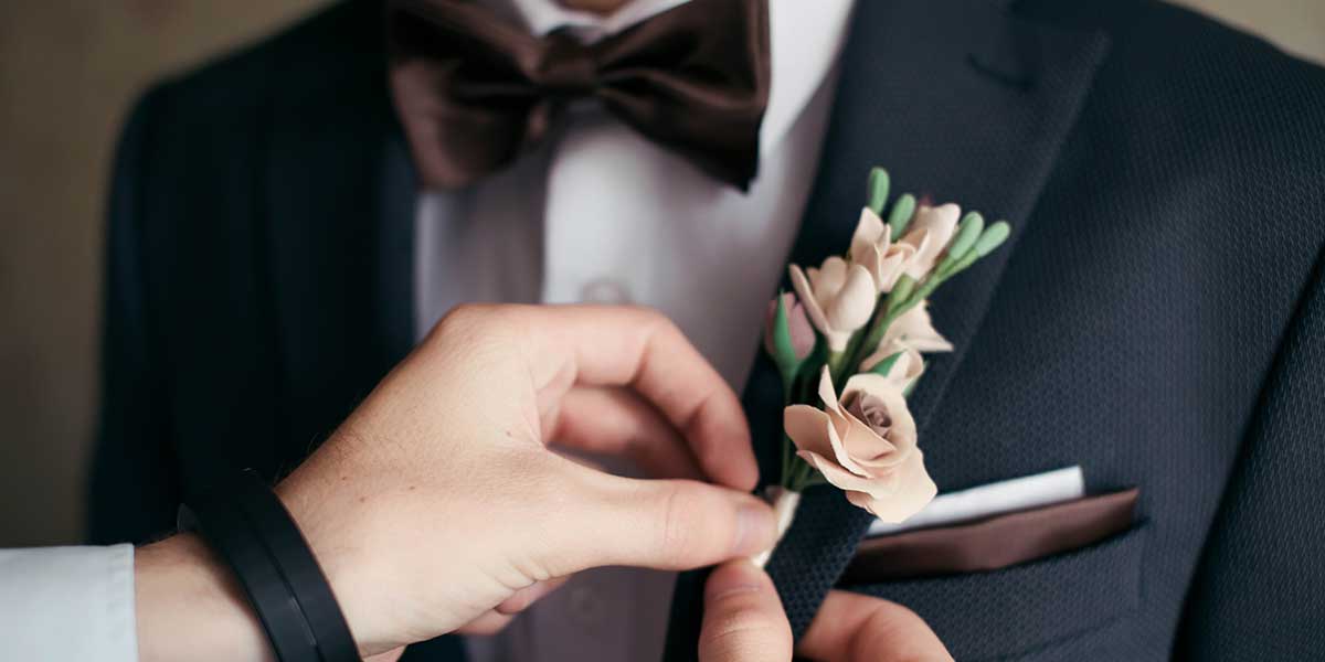 結婚式を迎える新郎の胸元の花を整える女性の手