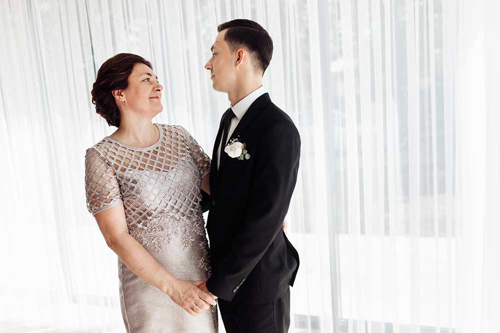 the groom hugs his mother and holds her hand. mom and son at the wedding. son's wedding. happy mom on wedding day