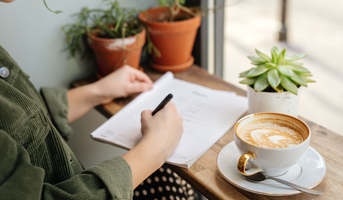 コーヒーを飲みながらメッセージを紙に書く女性の手元