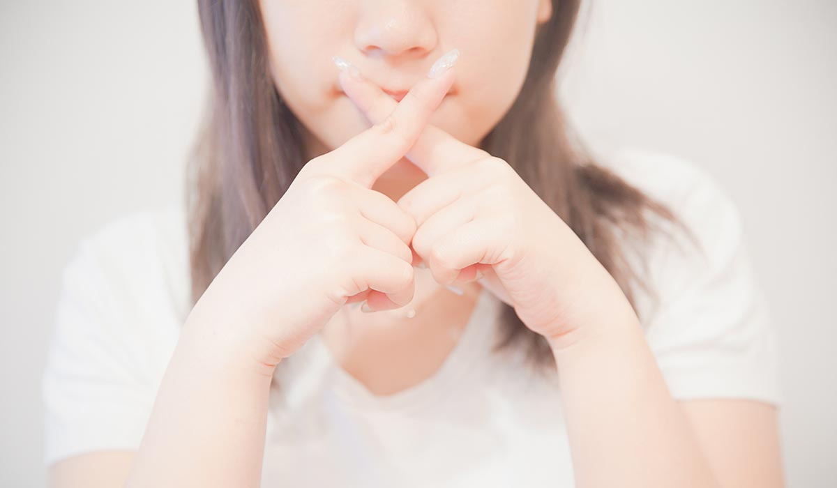 口元でバツのしぐさをする女性