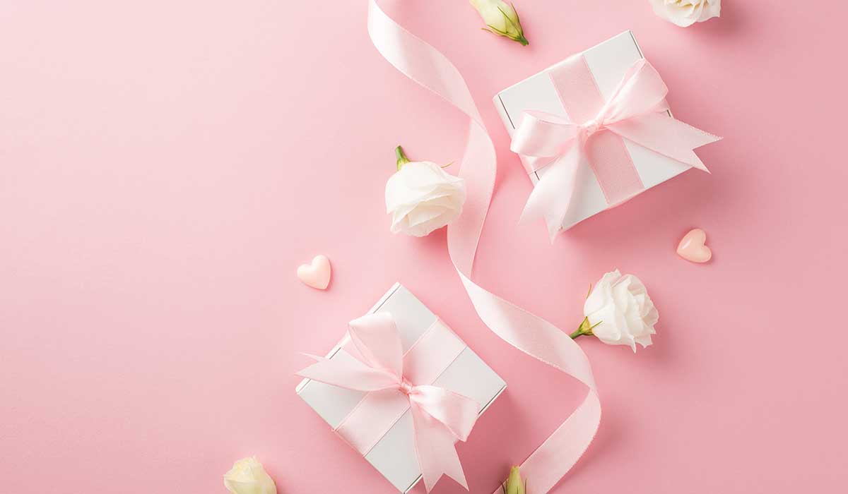 ピンクの背景にピンクのリボンが付いたプレゼントが2つとバラの花が置かれている