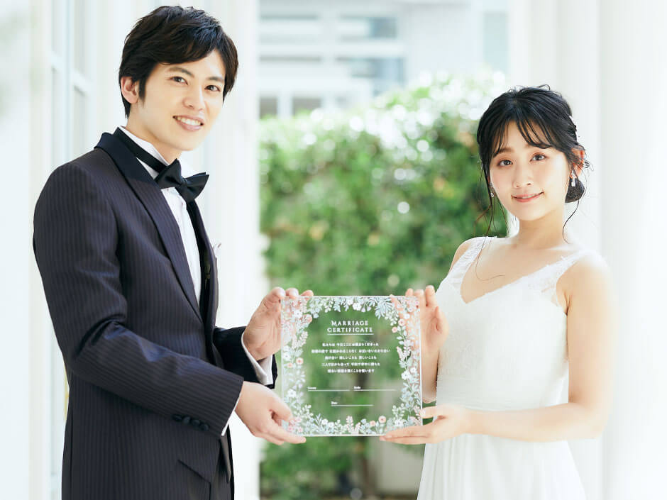 透明なアクリルに花柄入り結婚証明書を掲げている新郎新婦