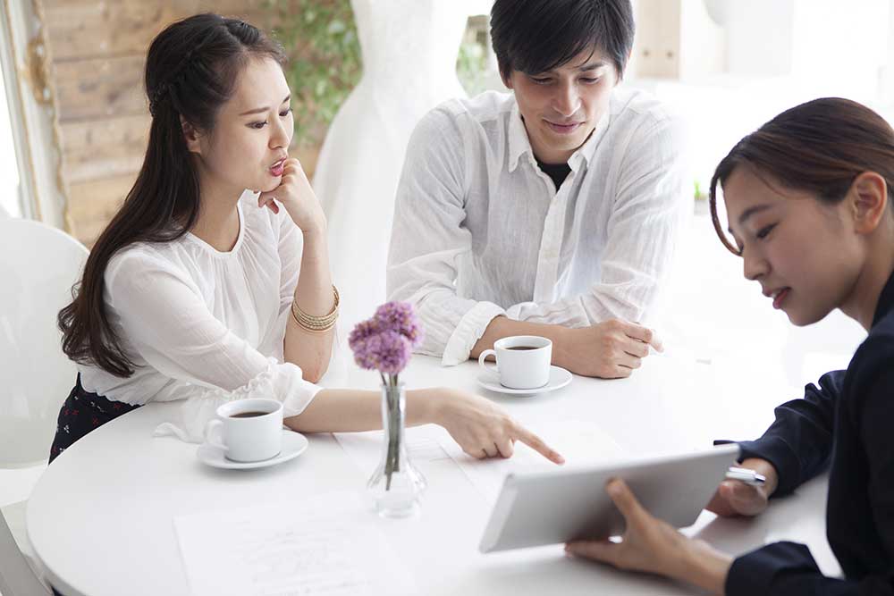 ウェディングプランナーとタブレットを見ながら相談するカップル