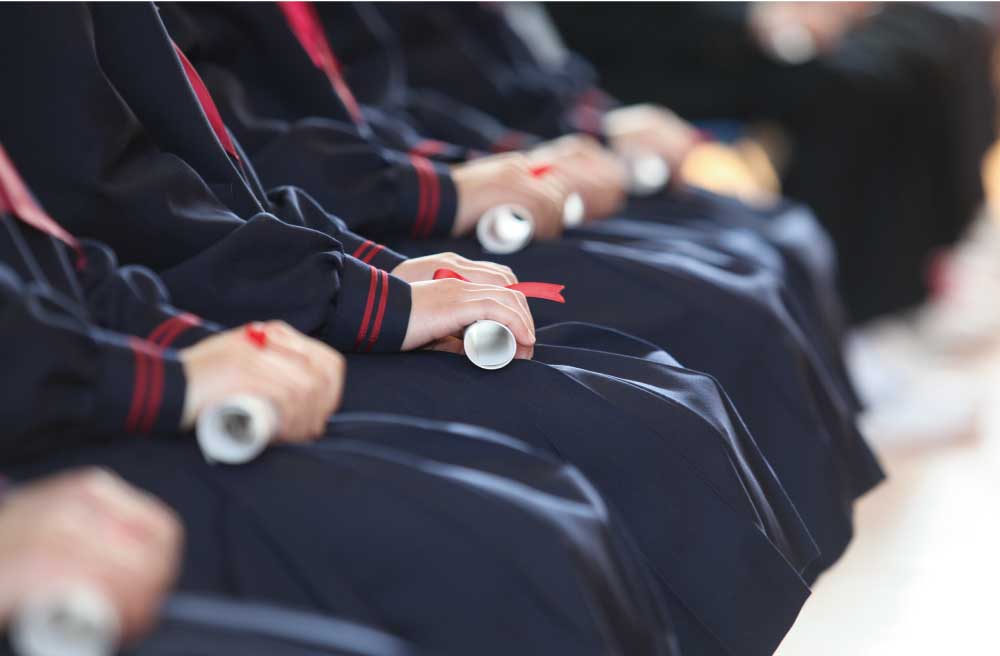 卒業証書を握って並んで座っている女子学生